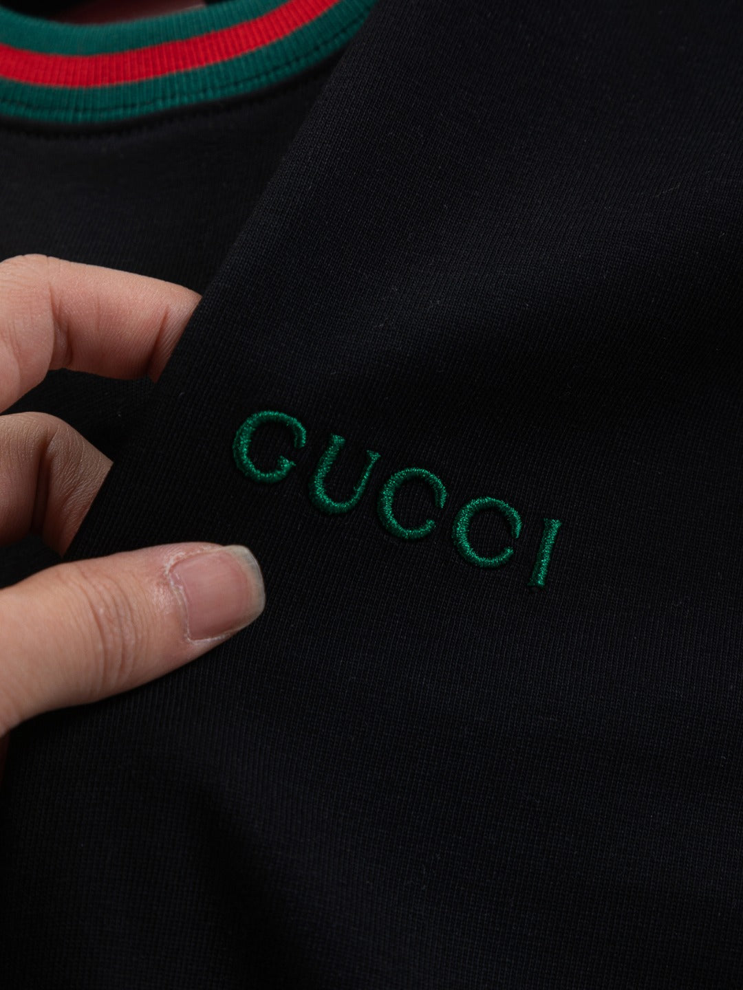 Hand holding Gucci T-shirt fabric, green embroidered "GUCCI" on black