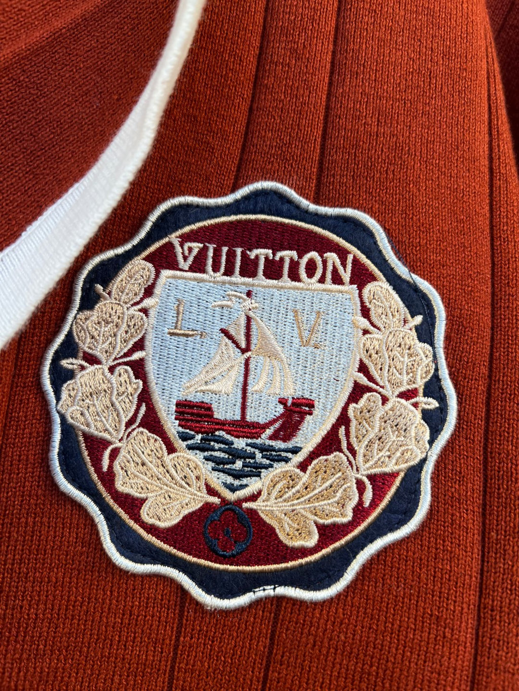 Rust red cardigan featuring an embroidered nautical crest patch with white border