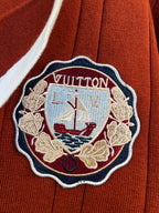 Rust red cardigan featuring an embroidered nautical crest patch with white border
