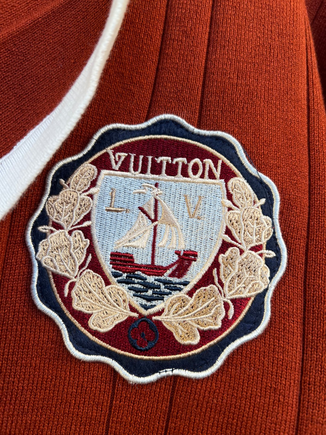 Rust red cardigan featuring an embroidered nautical crest patch with white border