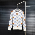 White knit sweater with blue GG motif and orange teddy bear designs.