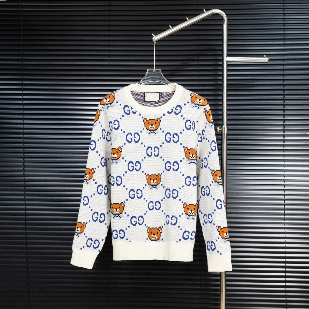 White knit sweater with blue GG motif and orange teddy bear designs.