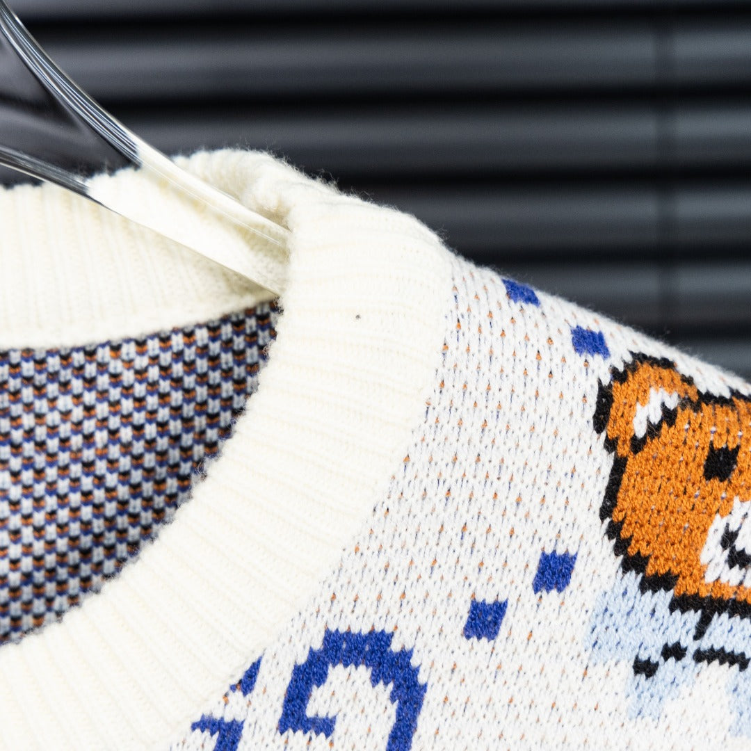 White knit sweater sleeve with blue dotted GG pattern and orange teddy bear graphic.