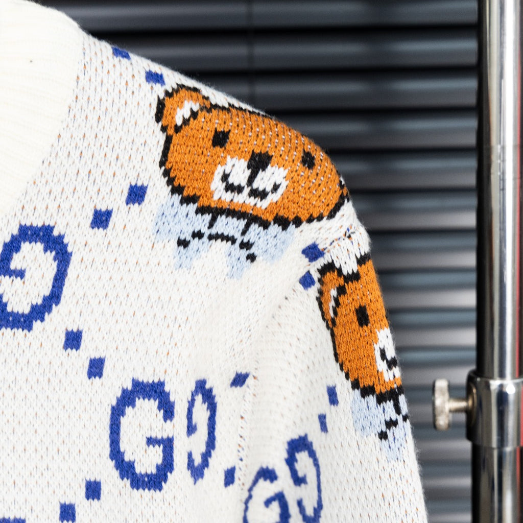 White knit sweater with orange teddy bear face graphic and blue dotted GG motif.