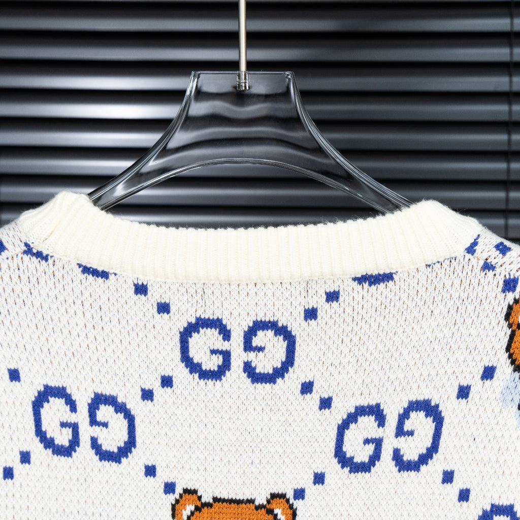 White knit sweater with blue GG motifs and orange teddy bear pattern across back.