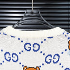 White knit sweater with blue GG motifs and orange teddy bear pattern across back.