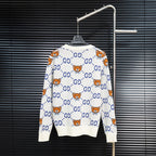 White knit sweater with blue GG motifs and orange teddy bear pattern, back view.