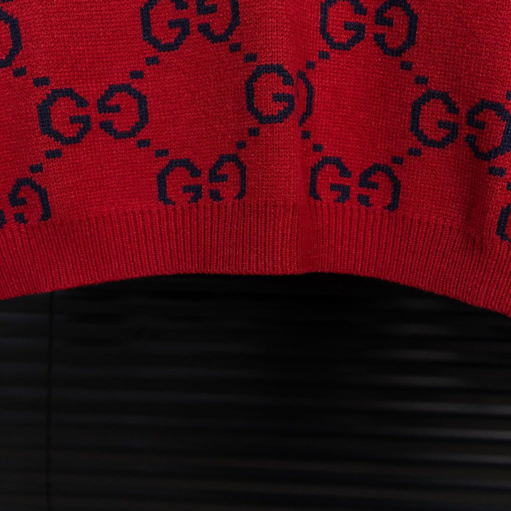 Bottom hem of navy knit sweater with red GG monogram pattern and ribbed edge.