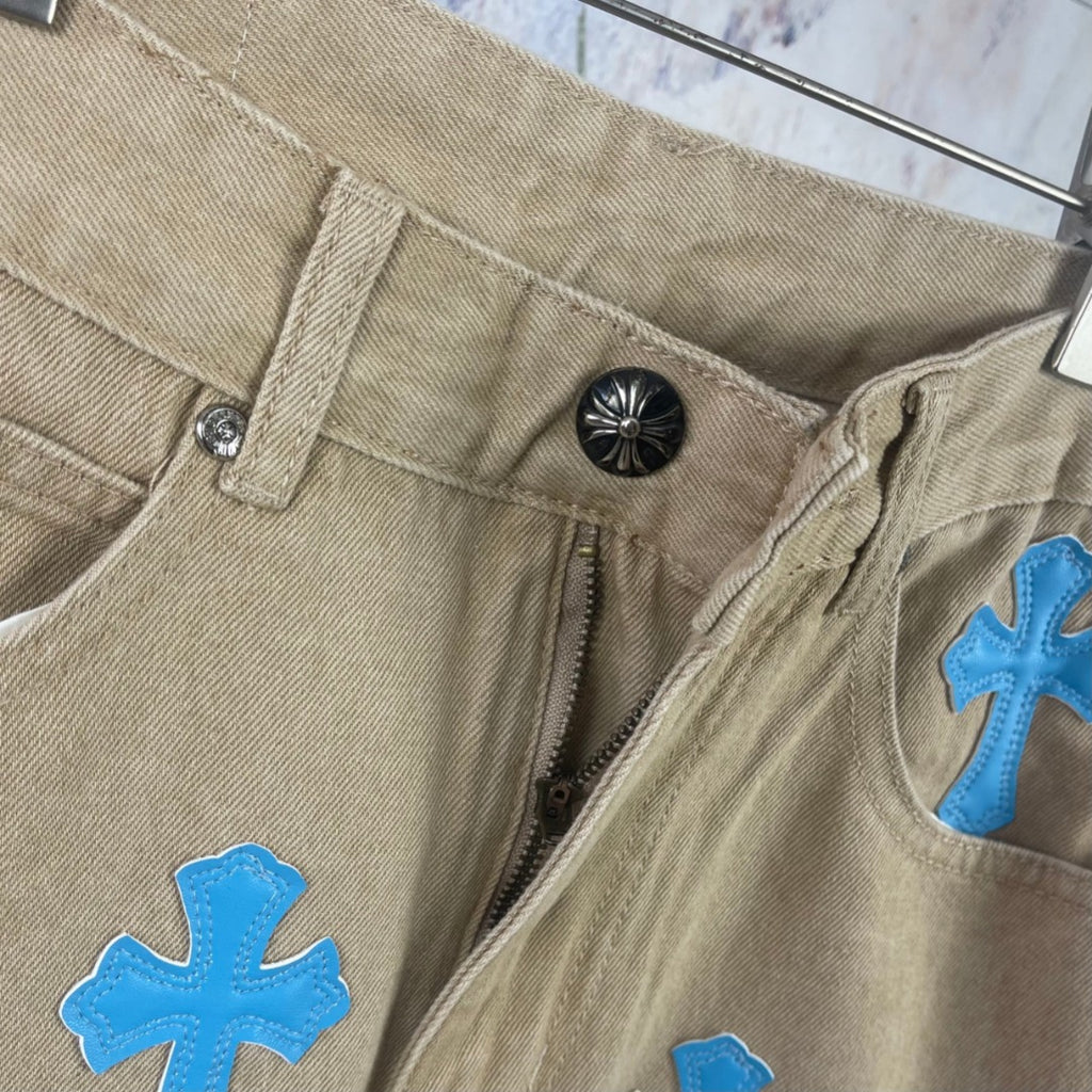 Close-up of beige pants waistband with button, zipper, and blue cross-heart patch