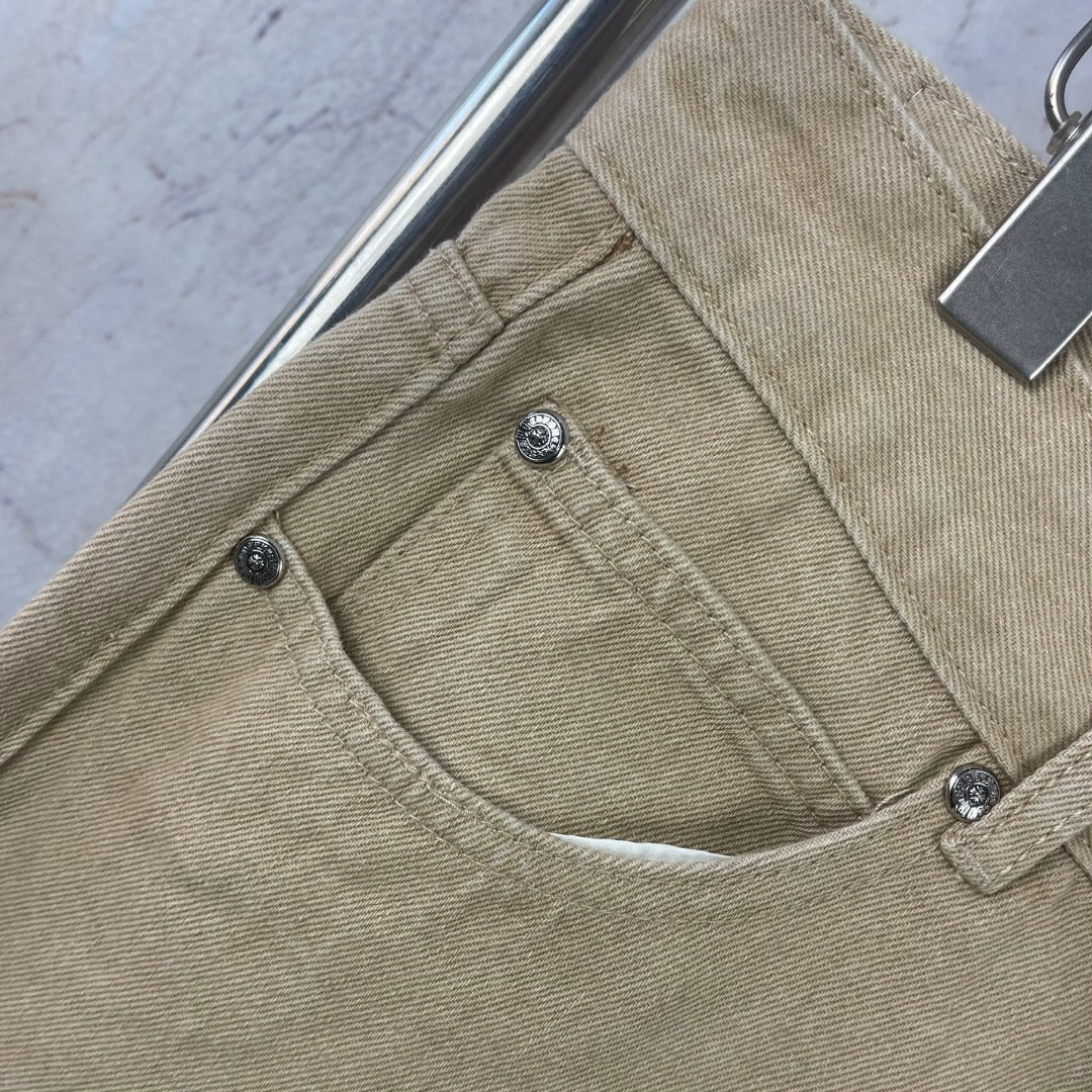 Beige pants front close-up with belt loops, button closure, and stitched curved pocket