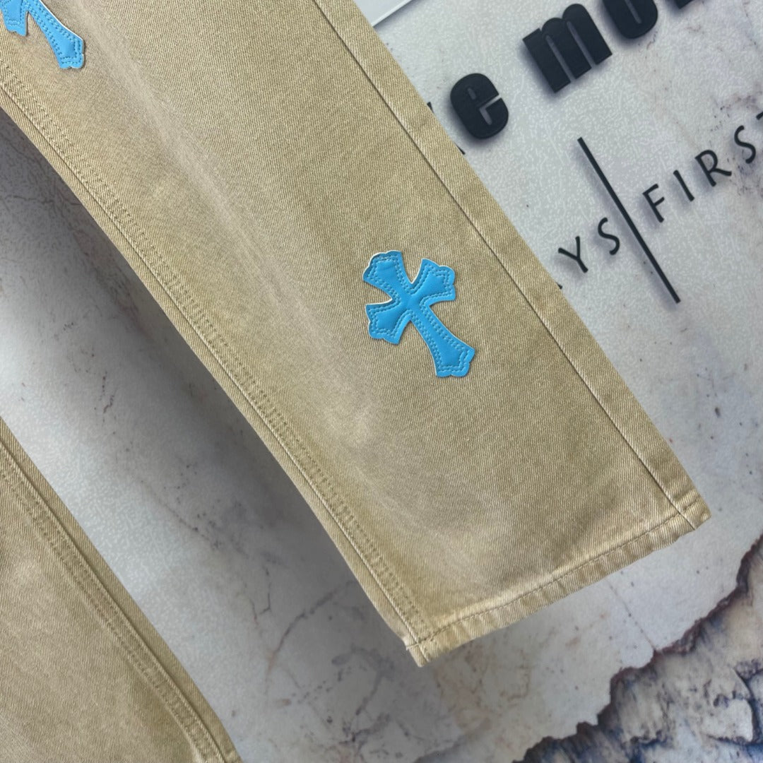 Beige pants leg with blue cross-heart patch near hem, straight cut