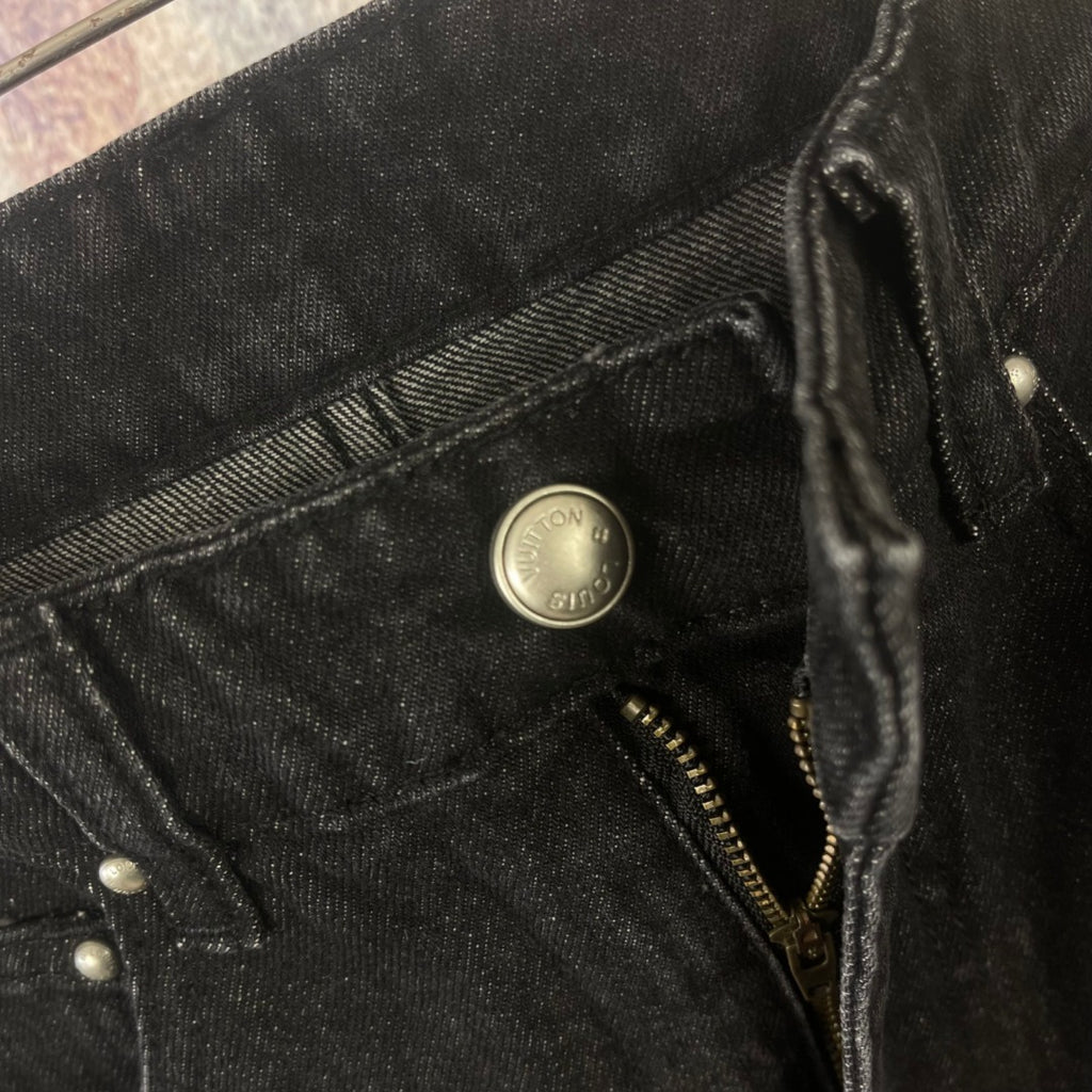 Close-up of black denim pocket with metal button and zipper detail