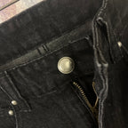 Close-up of black denim pocket with metal button and zipper detail