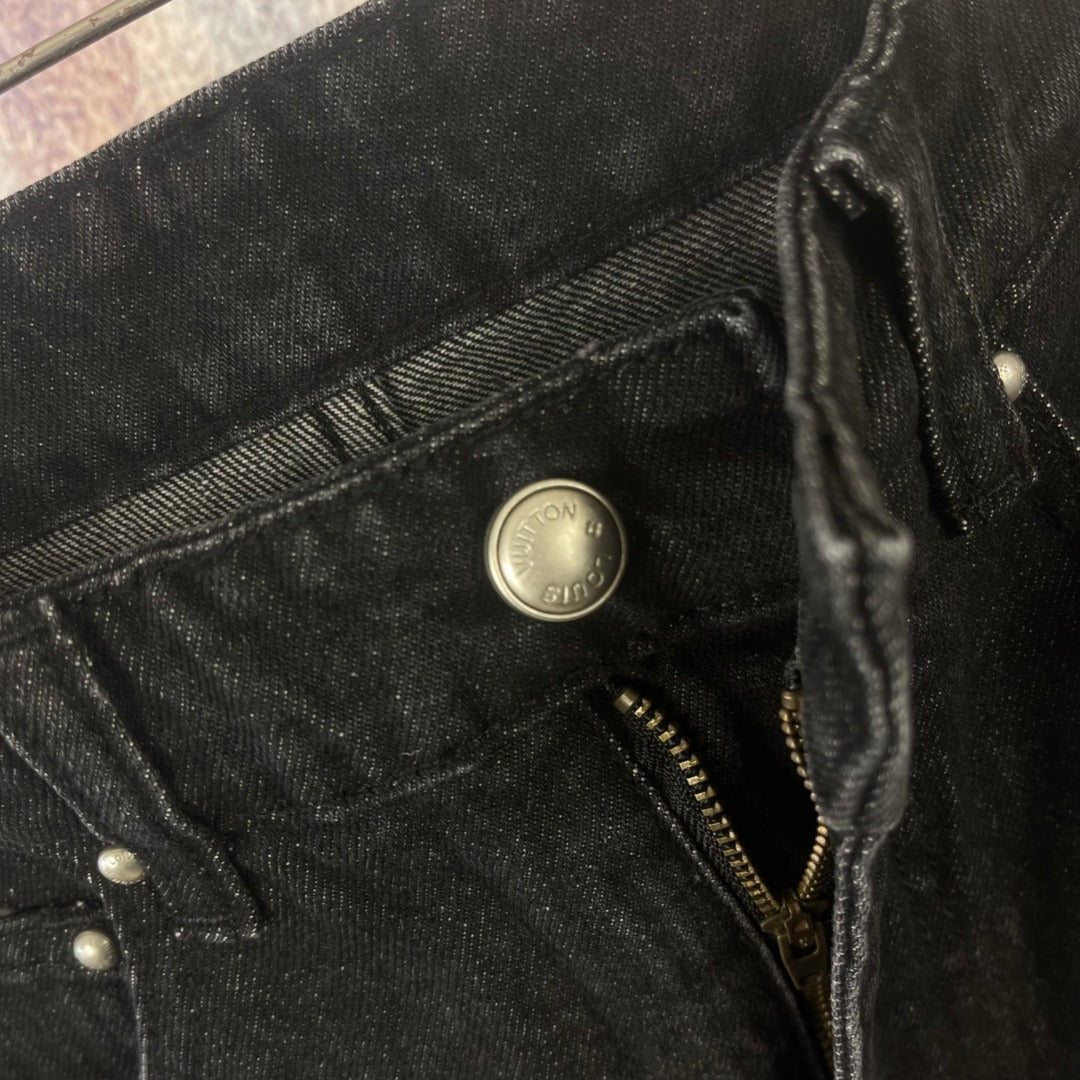 Close-up of black denim pocket with metal button and zipper detail
