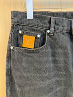 Front pocket detail on dark denim pants with LV monogram label.
