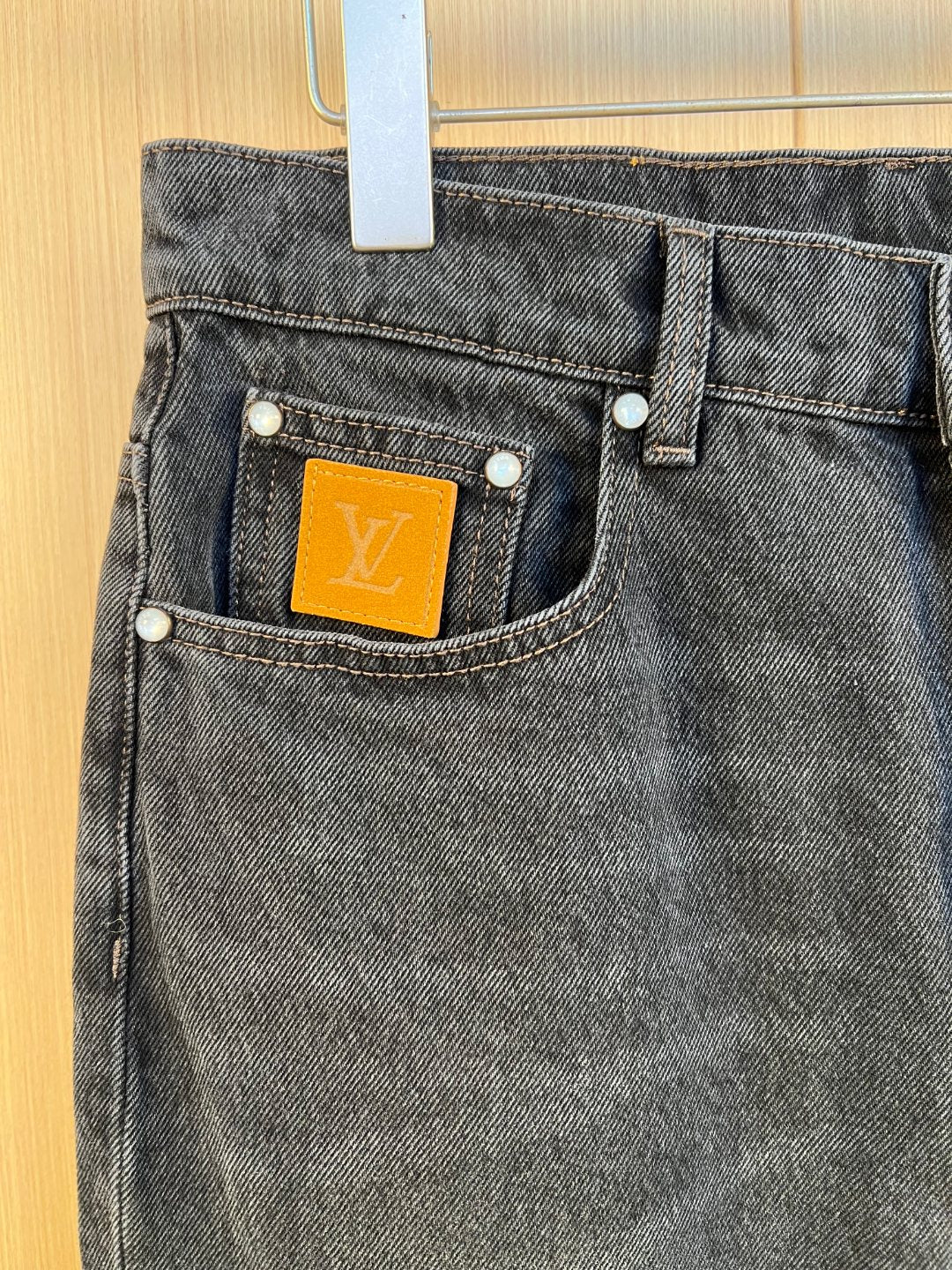 Front pocket detail on dark denim pants with LV monogram label.