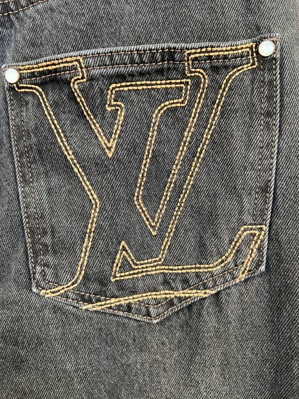 Back pocket of dark denim pants with gold LV-stitched monogram.