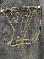 Back pocket of dark denim pants with gold LV-stitched monogram.