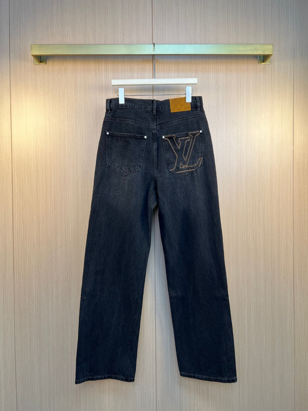 Dark denim pants with front pockets and LV logo patch at hip.