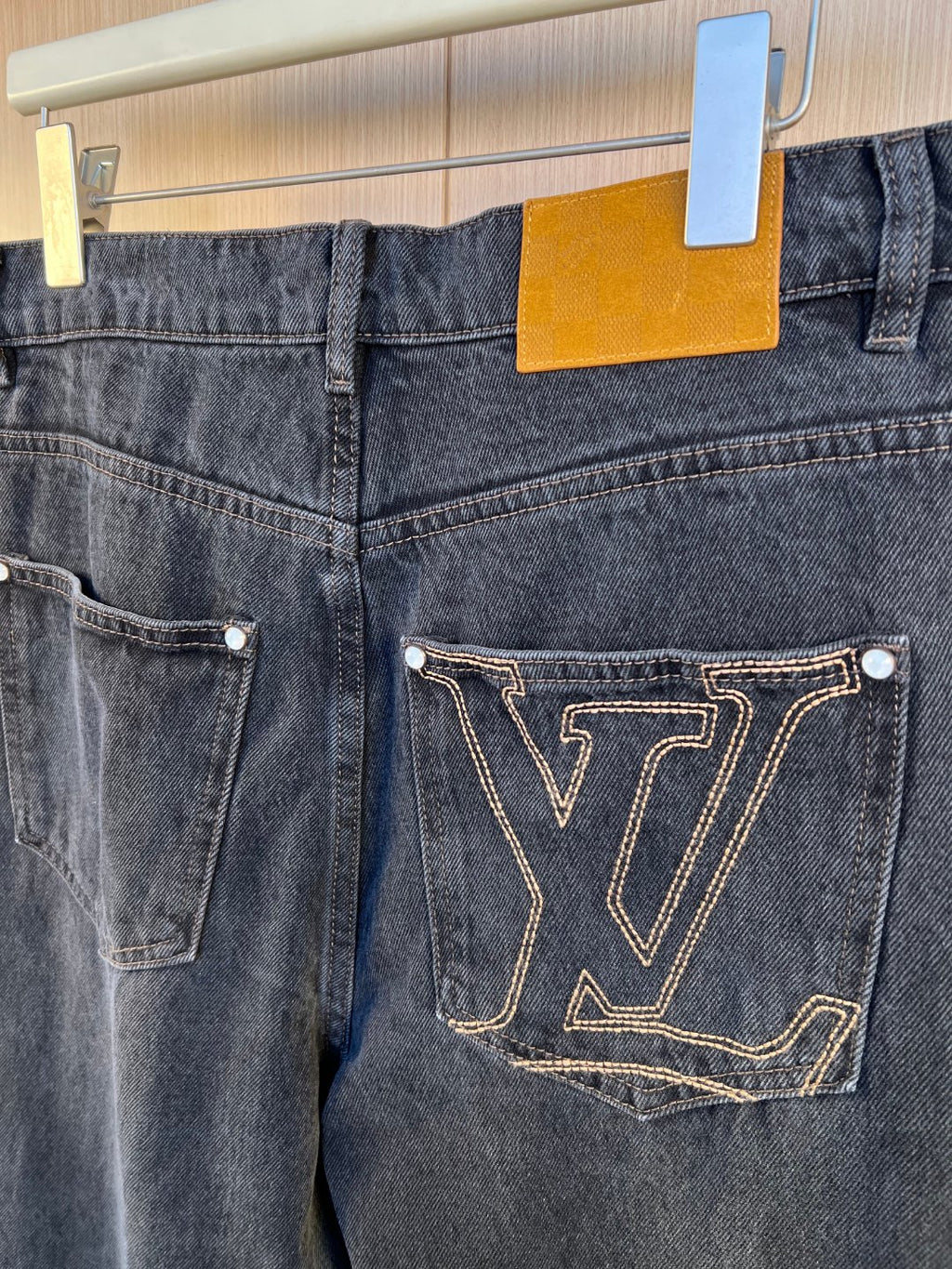 Dark denim pants back view with large gold LV-stitched pocket design.