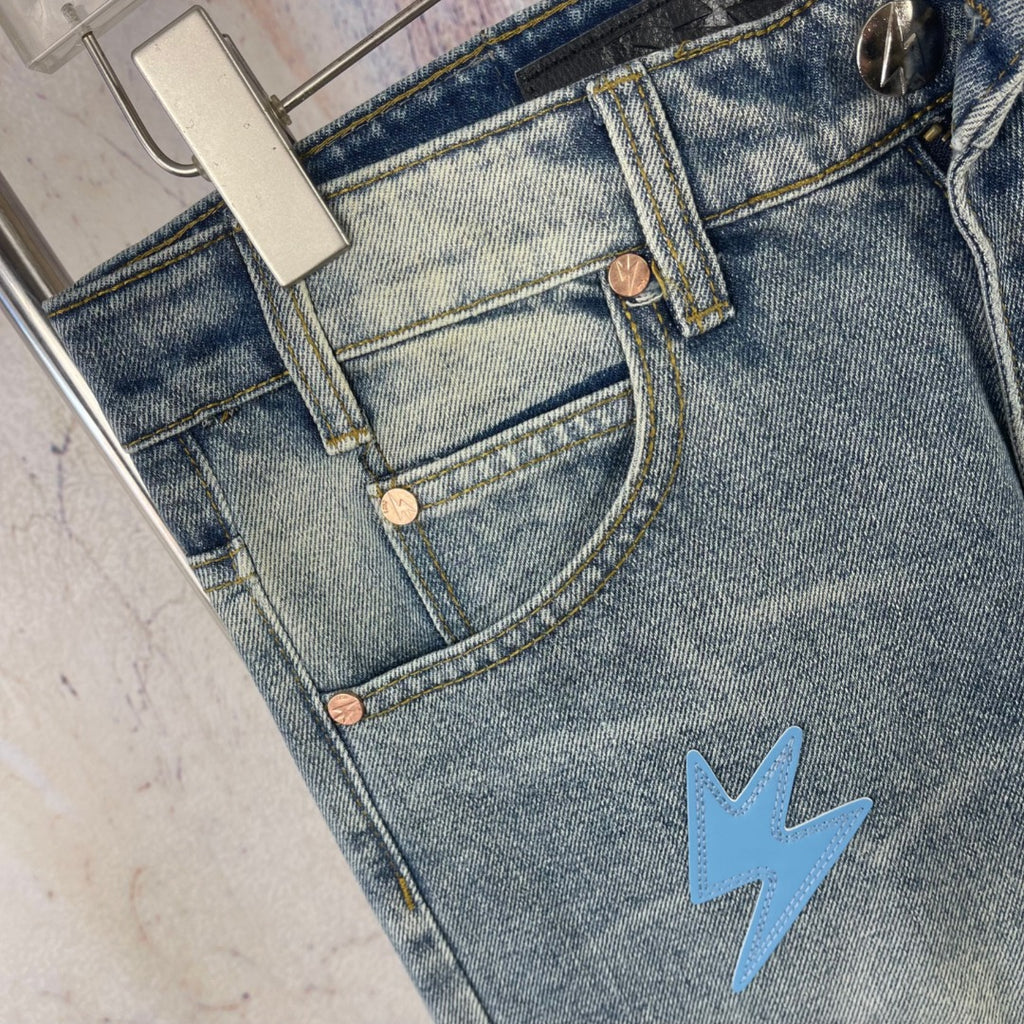 Light blue denim jeans front with brass buttons and light blue lightning patch