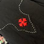 Black denim jacket collar close-up with red floral emblem and rhinestone border