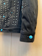 Dark denim jacket cuff with silver studs and blue accent button detail.