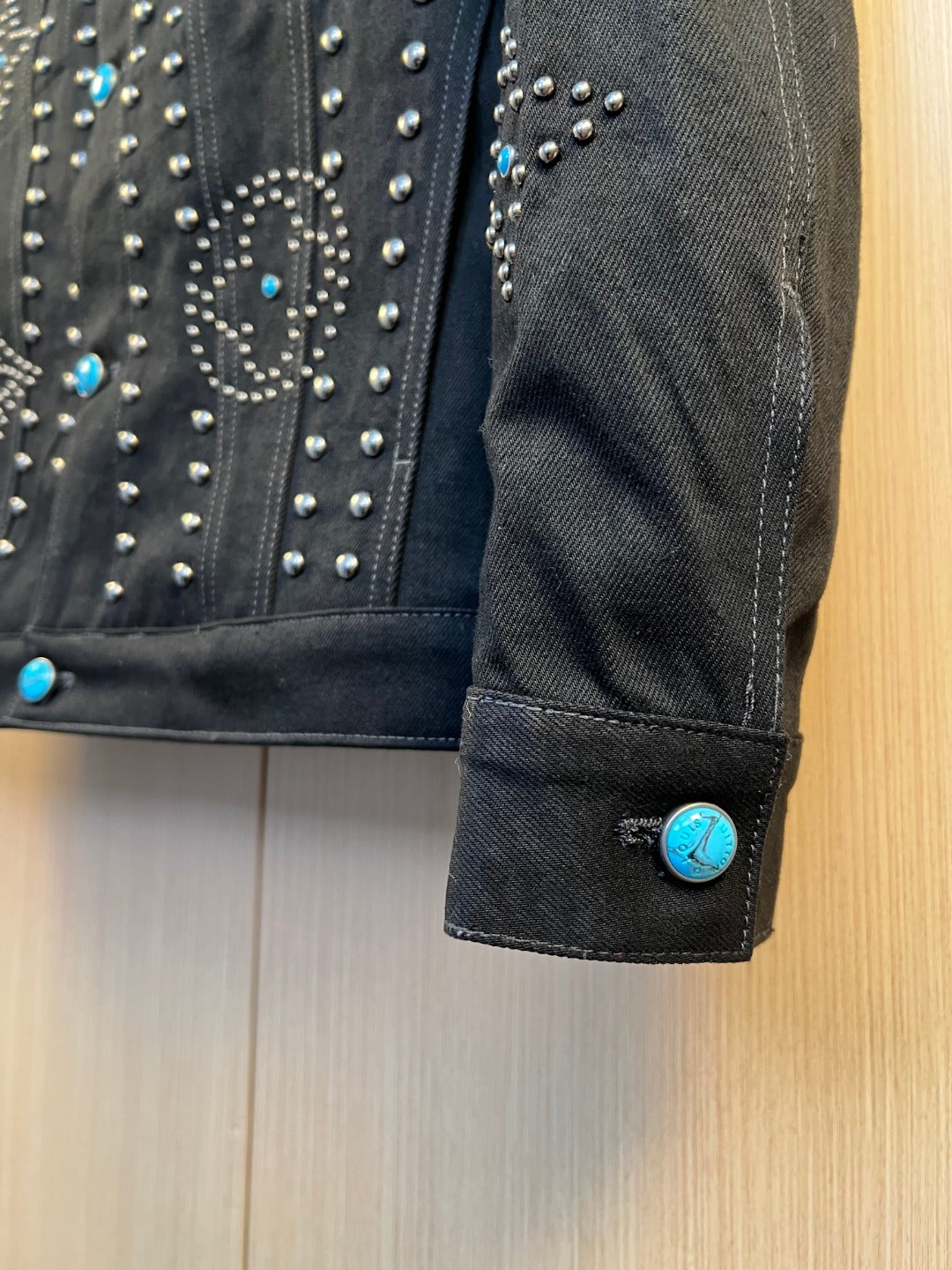 Dark denim jacket cuff with silver studs and blue accent button detail.