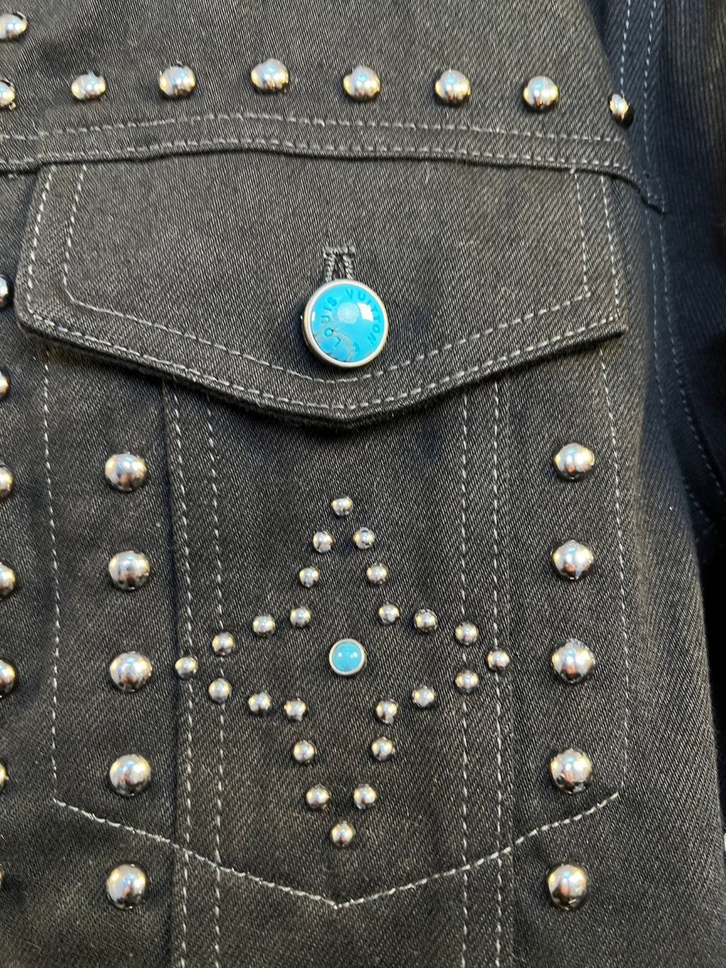 Dark denim jacket chest panel with silver studs and blue rhinestone accents.