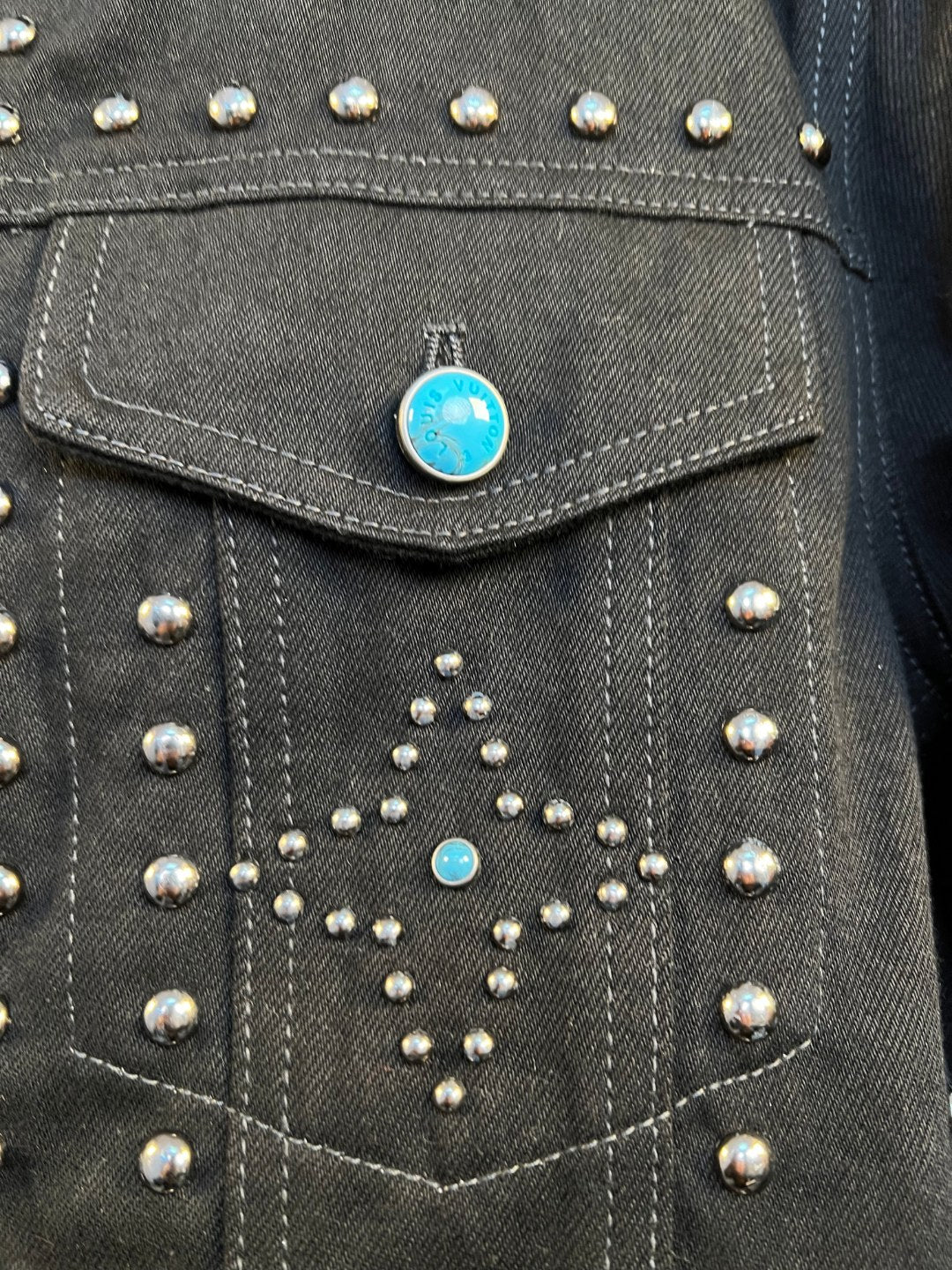 Dark denim jacket chest panel with silver studs and blue rhinestone accents.