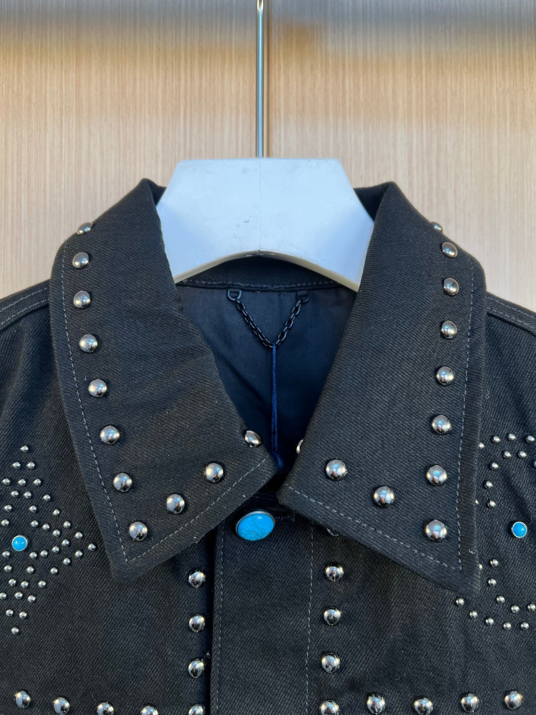 Dark denim jacket collar with silver studs and blue button accent at neckline.