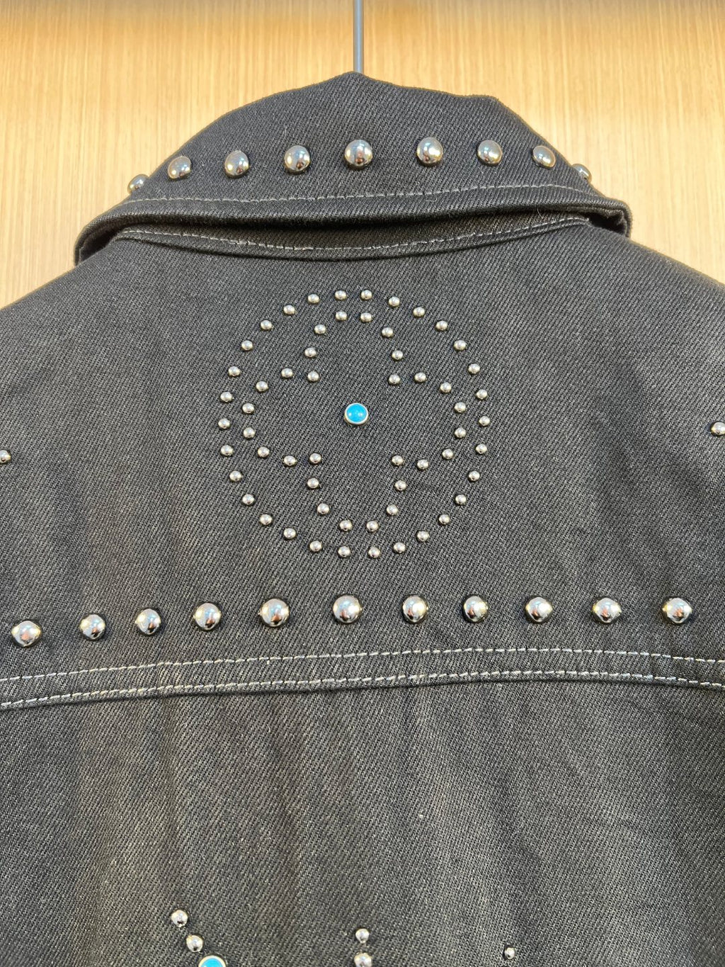Dark denim jacket back yoke with studded diamond motif and blue rhinestone dot.