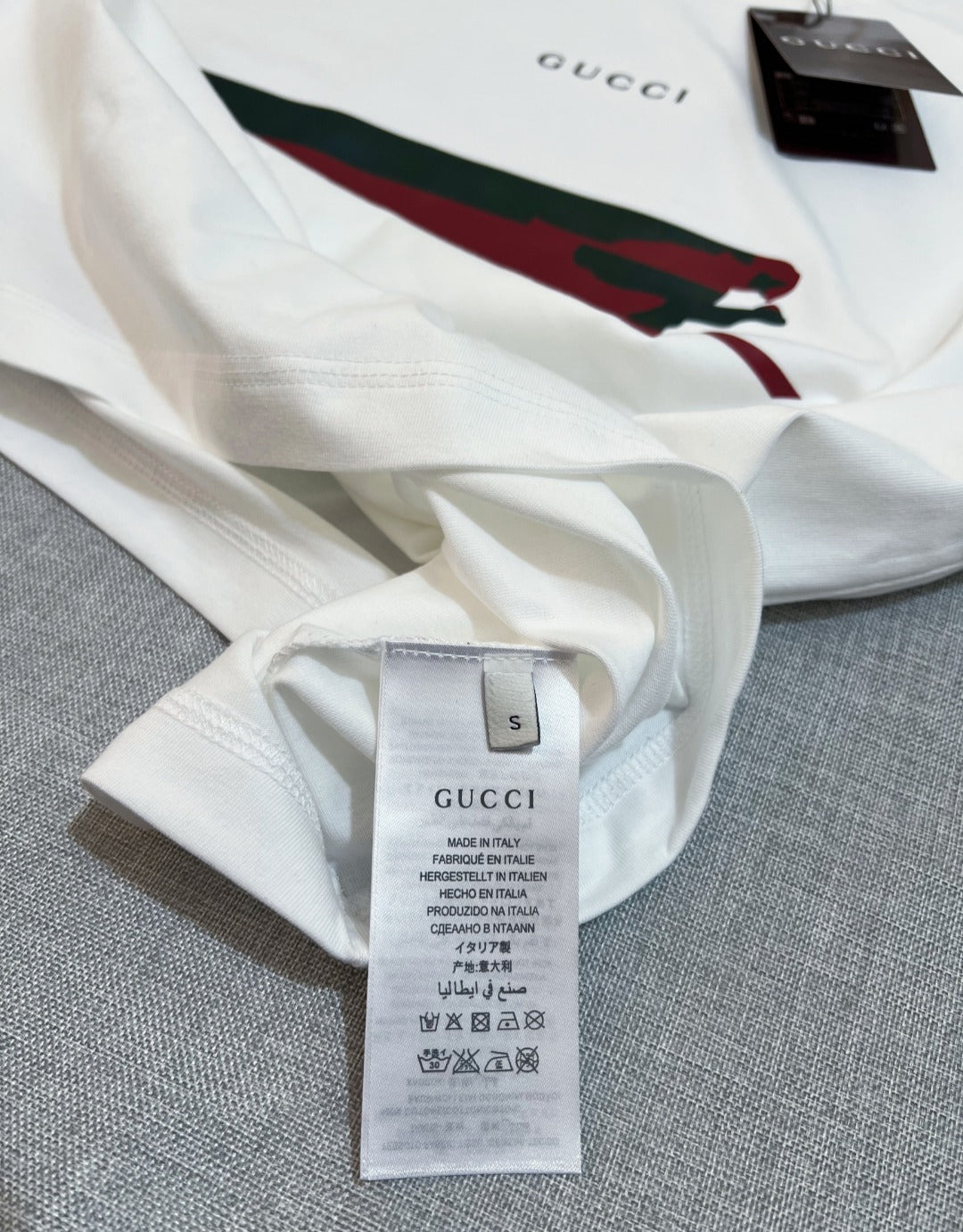 White Gucci T-shirt fabric close-up with size label and partial red/green graphic