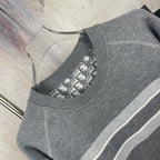 Close-up side view of gray crewneck sweater with striped trim and ribbed neckline