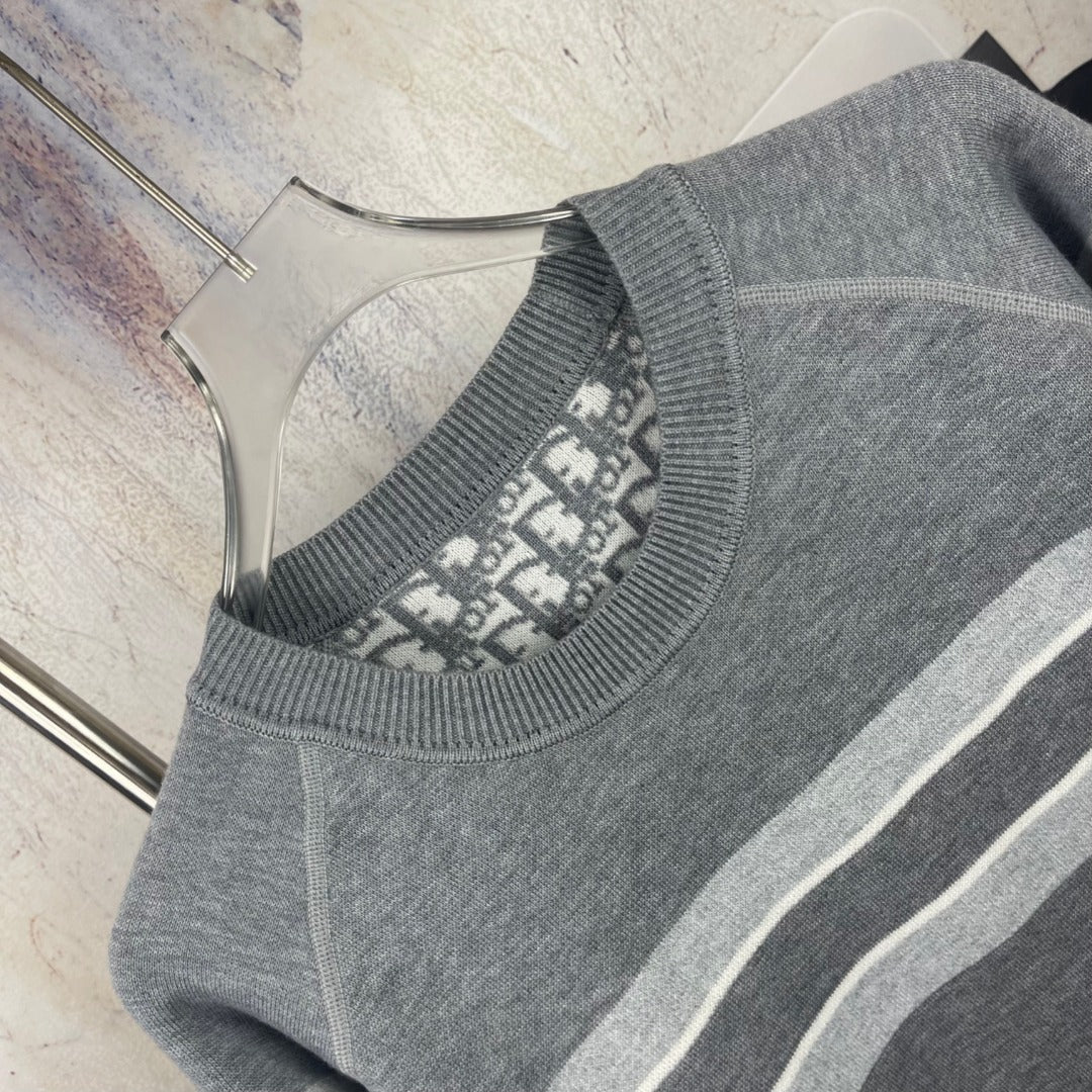 Close-up side view of gray crewneck sweater with striped trim and ribbed neckline