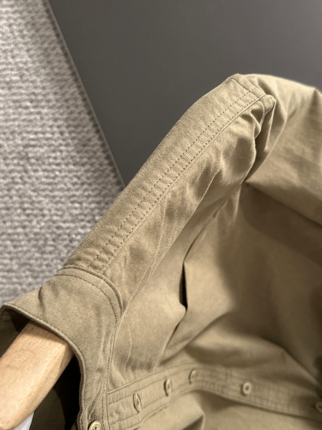 Long-sleeve shirt sleeve and shoulder detail with stitched seams, olive-brown.