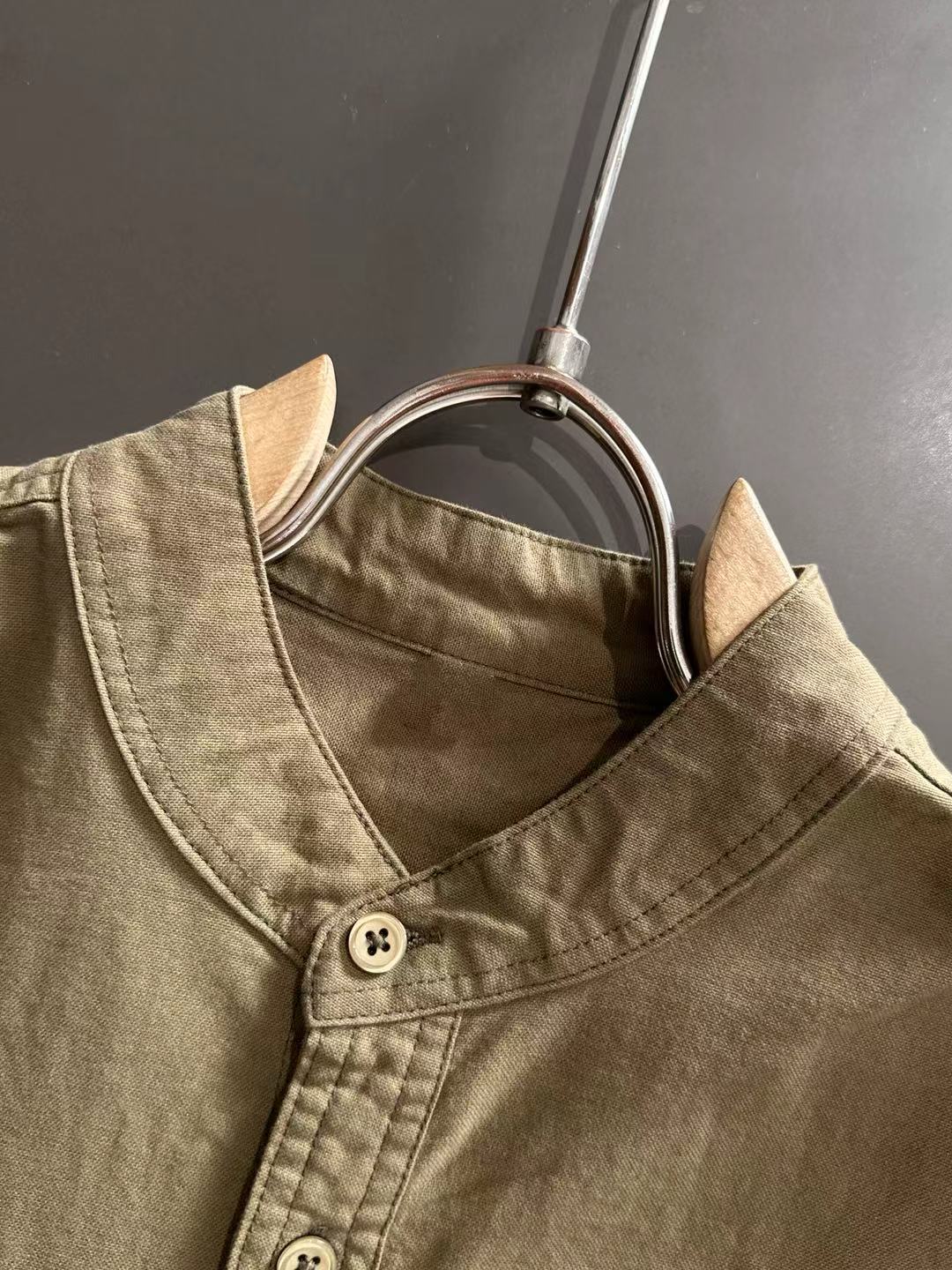Long-sleeve shirt neckline close-up with front buttons, olive-brown canvas.