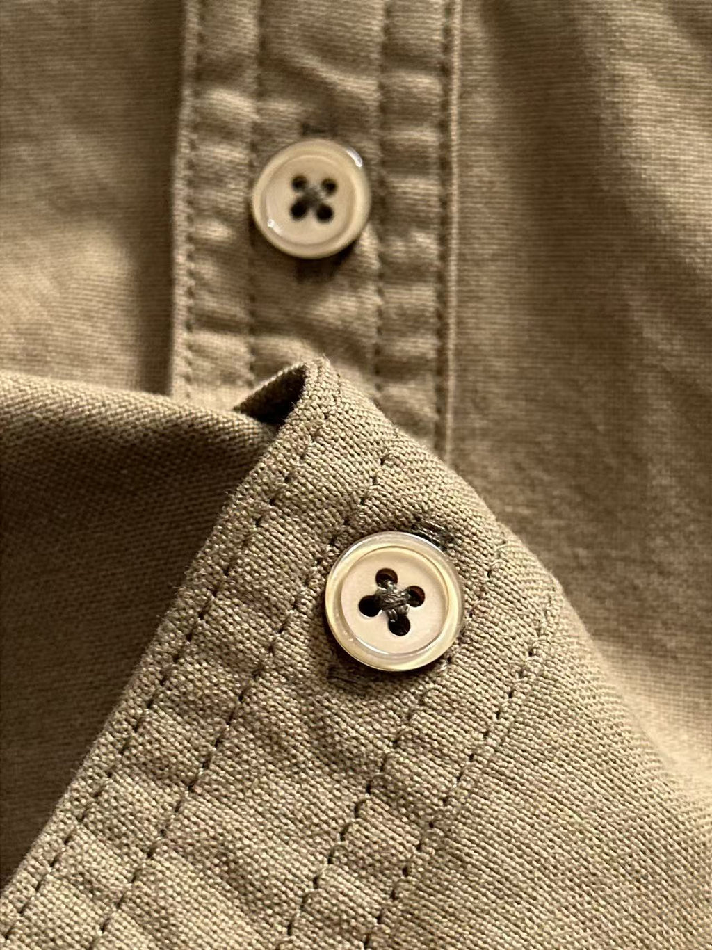 Shirt cuff button close-up with looped stitching, olive-brown.