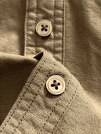 Shirt cuff button close-up with looped stitching, olive-brown.