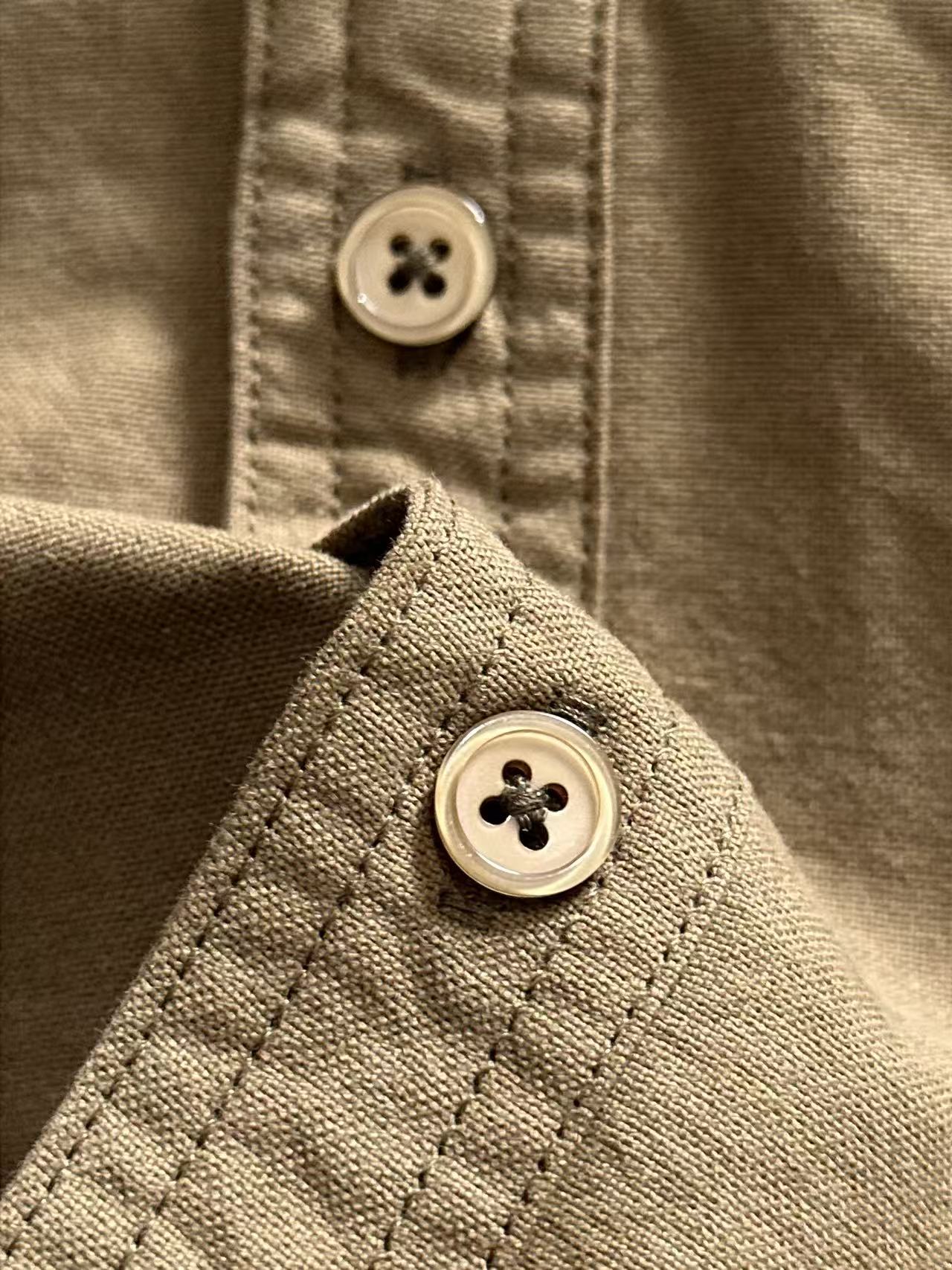 Shirt cuff button close-up with looped stitching, olive-brown.
