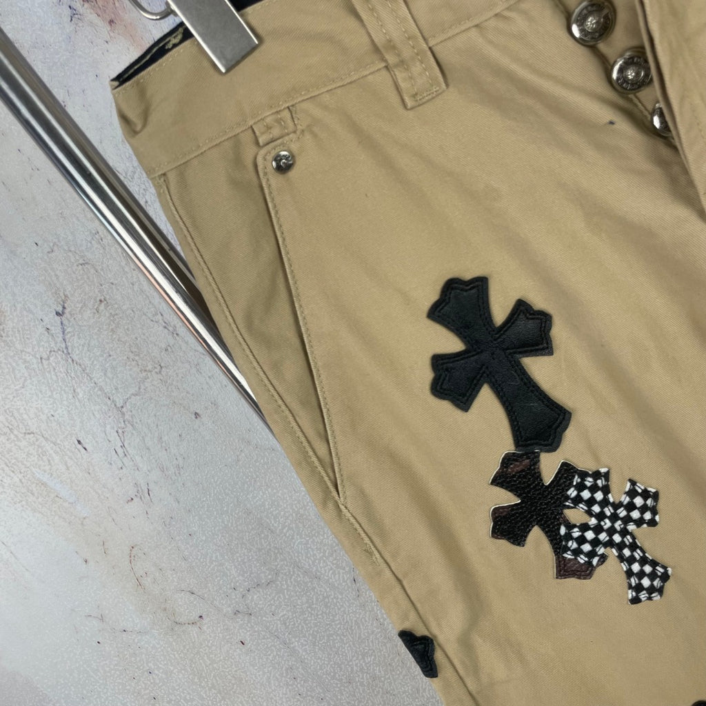 Tan pants with black cross patch embroidery on leg, front hem close-up.