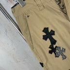 Tan pants with black cross patch embroidery on leg, front hem close-up.