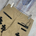 Tan cargo-style pants with multiple black cross appliques and belt loops, back view.