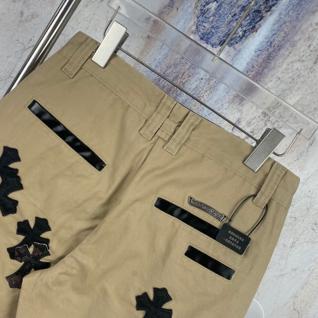 Tan cargo-style pants with multiple black cross appliques and belt loops, back view.