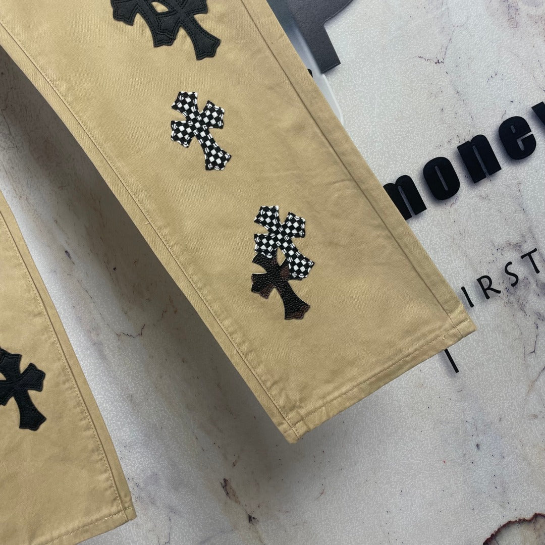 Tan pants with black cross patch embroidery on lower legs, angled view.