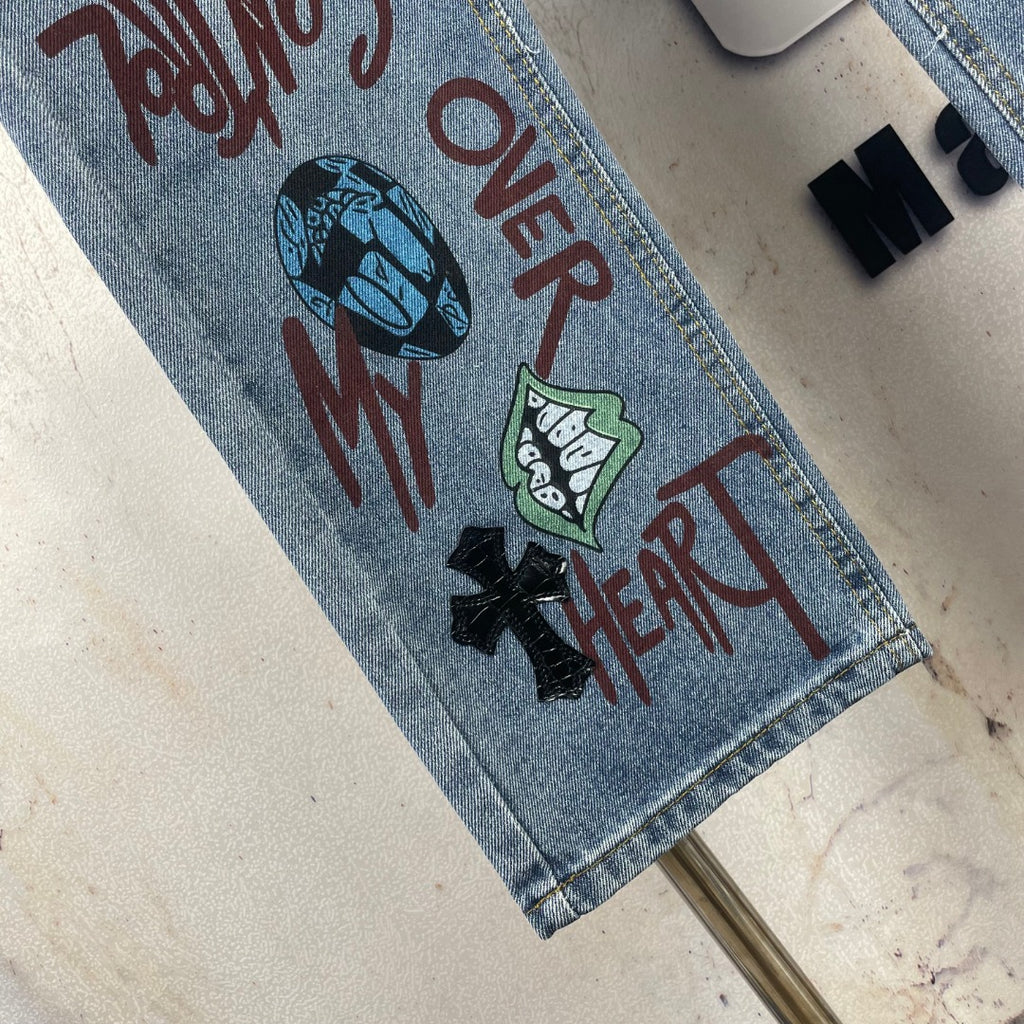 Light blue denim pants hem close-up with colorful text and black heart-and-cross graphic