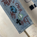 Light blue denim pants hem close-up with colorful text and black heart-and-cross graphic