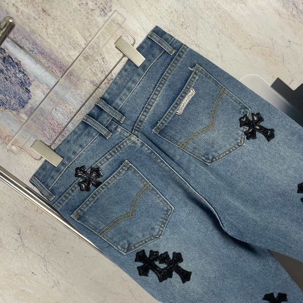 Light blue denim pants flat lay showing front pockets and black cross appliques