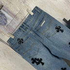 Light blue denim pants flat lay showing front pockets and black cross appliques