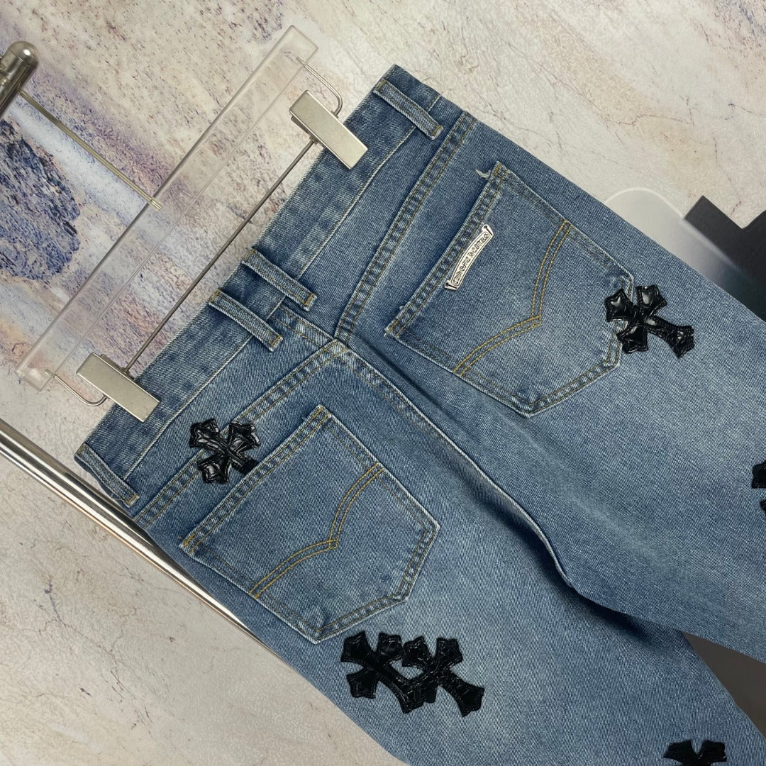 Light blue denim pants flat lay showing front pockets and black cross appliques